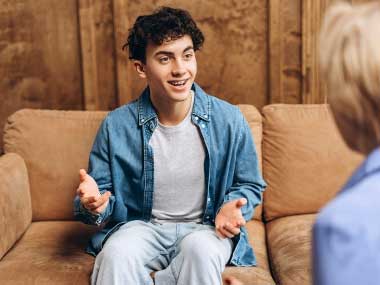 A young man sitting on a couch talking and gesturing during a therapy session.